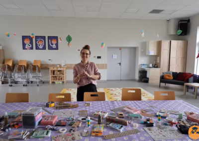 Sala w CAL Jagodno przygotowana do warsztatów kart afirmacyjnych, stół z materiałami plastycznymi i prowadząca w tle